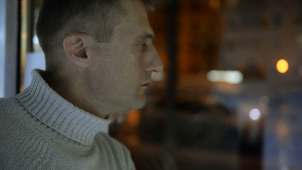 Depressief man naast het venster op de achtergrond van een avond street, auto's en verlichting - Video