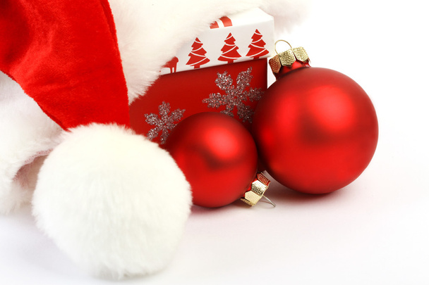 Καπέλο Santa με pom pom drape κόκκινο χριστουγεννιάτικο κουτί με κόκκινη διακόσμηση Χριστούγεννα και δύο κόκκινες μπάλες Χριστούγεννα ματ σε άσπρο φόντο. - Φωτογραφία, εικόνα