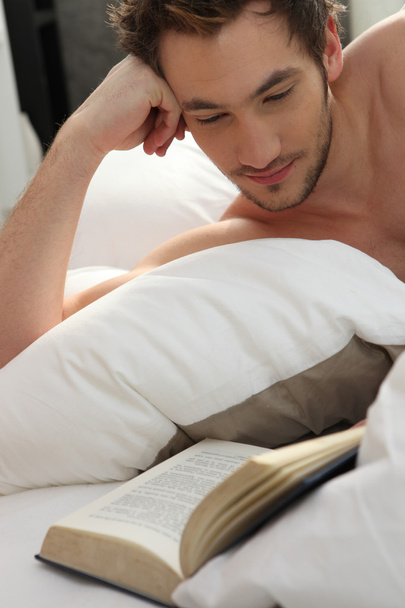 Young man bare-chested reading in bed - Foto, Imagem