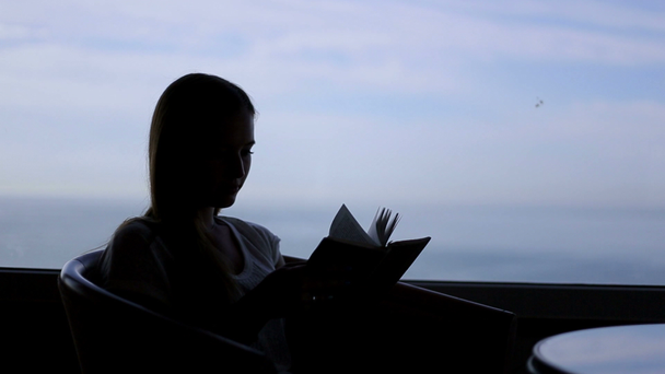 silhouette of young beautiful girl sits in a cafe with panoramic views of atlantic ocean. Morning with a book, notepad, reading, thinking - Footage, Video