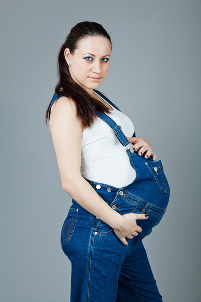 Portrait of pregnant brunette woman on grey background. - 写真・画像