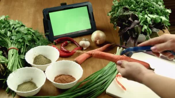 The woman cleans carrot and watches the recipe in the tablet - Footage, Video
