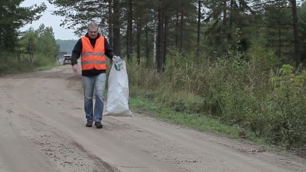 Mężczyzna z telefonu komórkowego i torby plastikowe butelki na drodze w lesie - Materiał filmowy, wideo