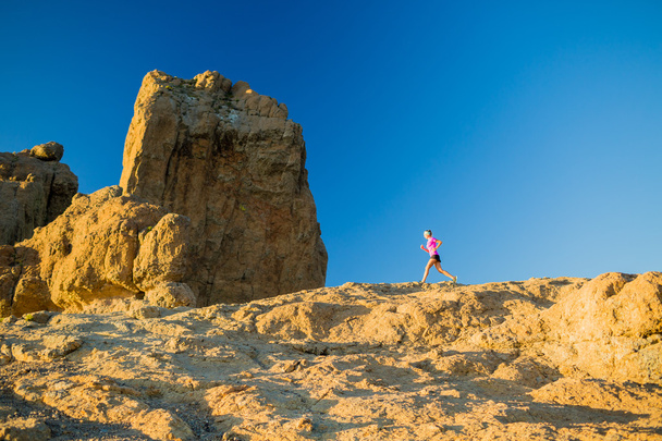 Mujer corriendo sobre montañas rocosas, entrenando y ejercitando
 - Foto, Imagen