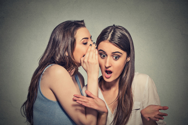 Girl whispering into woman ear telling her shocking secret - 写真・画像