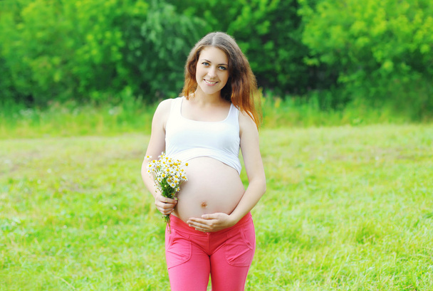 Feliz sorrindo jovem grávida com flores ao ar livre no summ
 - Foto, Imagem