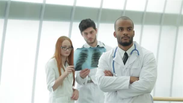 Egy fiatal orvos portréja röntgensugaras kézben két kolléga hátterével - Felvétel, videó