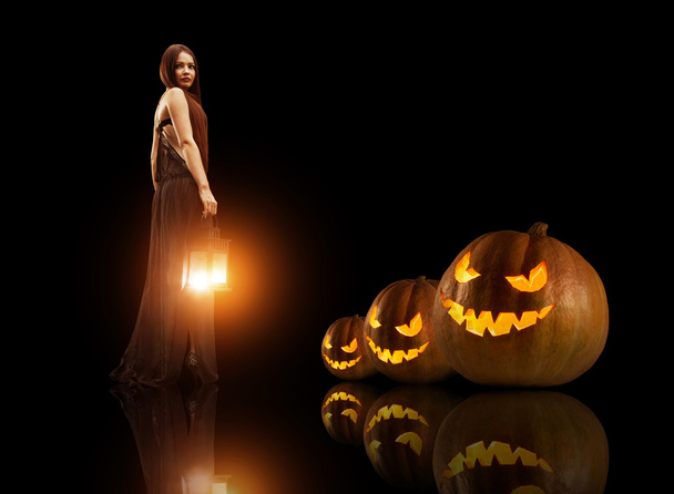 Beautiful witch with the magic lantern. Halloween pumpkins on th - Φωτογραφία, εικόνα
