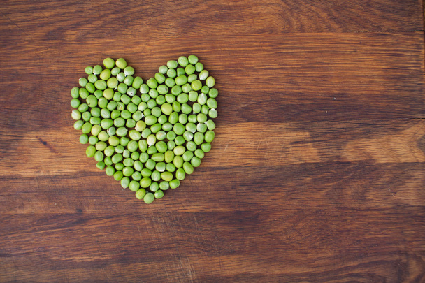 Corazón hecho de guisantes verdes frescos cultivados localmente sobre fondo de madera
 - Foto, Imagen