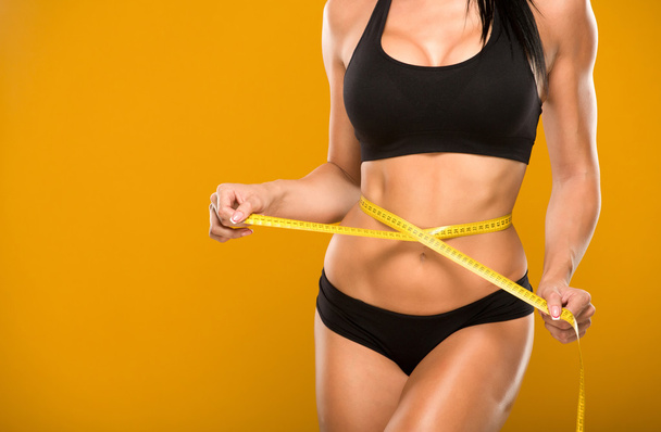 beautiful fitness model measures the waist on a yellow - Φωτογραφία, εικόνα