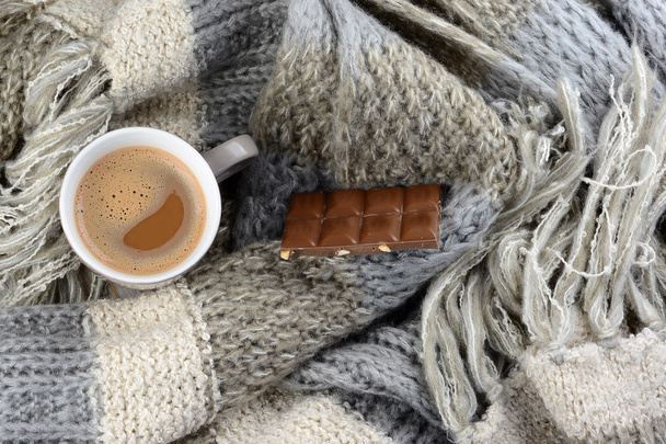 Hot chocolate in coffee mug  with a grey, ivory, ecru knitted scarf around it and chocolate bar - Photo, Image