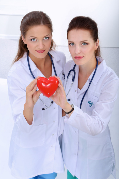 Kırmızı kalp taşıyan iki kadın doktor, beyaz arka planda izole edilmiş. - Fotoğraf, Görsel