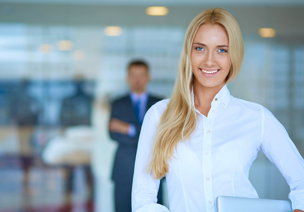 Portrait of young businesswoman with laptop in office with colleagues in the background - Foto, imagen