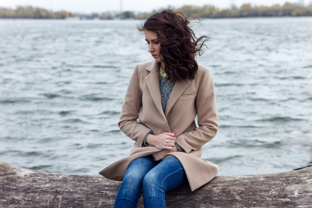 stylish girl in autumn coat sitting by the water - Фото, изображение