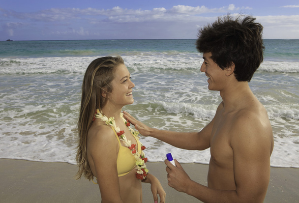 Молода пара на пляжі використовує сонячний блок
 - Фото, зображення