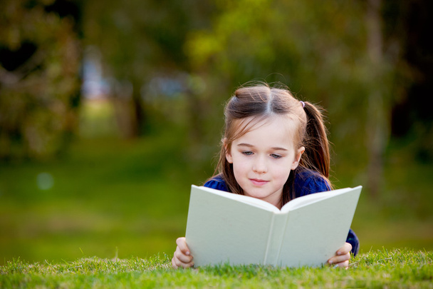 A little girl enjoying reading outdoors on the grass - Photo, Image