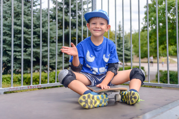 Cheeky young boy sitting on his skateboard - Photo, Image