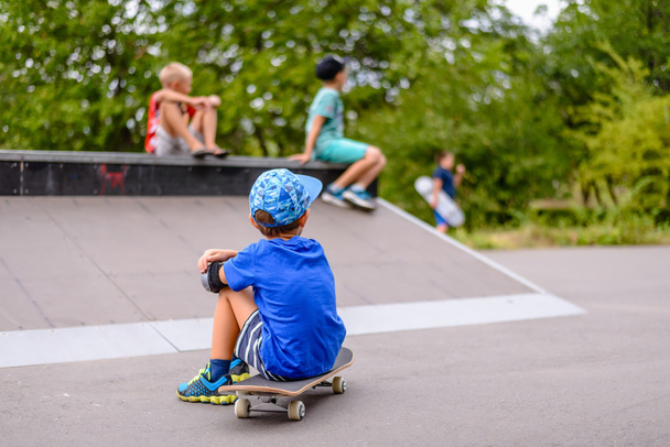 Menino sentado assistindo seus amigos no parque de skate
 - Foto, Imagem