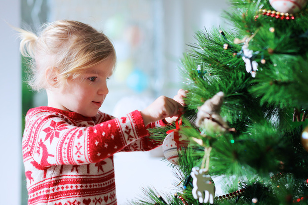 Beautiful little girl decorating christmas tree at home - Fotó, kép