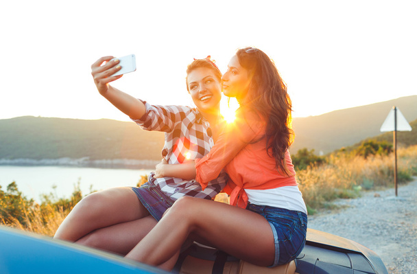 Duas meninas bonitas jovens estão fazendo selfie em um conversível
 - Foto, Imagem