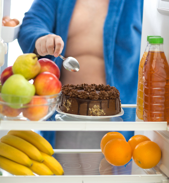 Obese guy prefer chocolate cake from fridge than fruit - Foto, Imagen