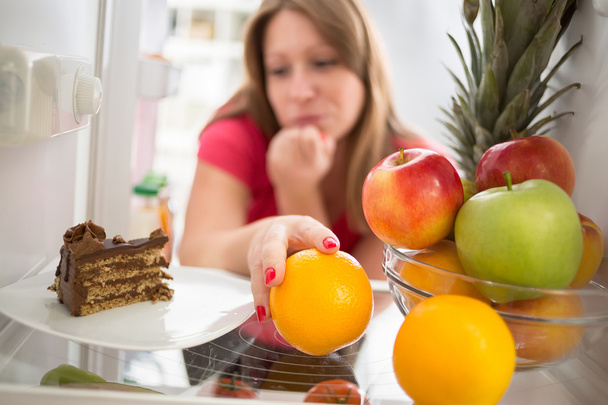 Woman hesitating whether to eat cake or orange - Фото, зображення
