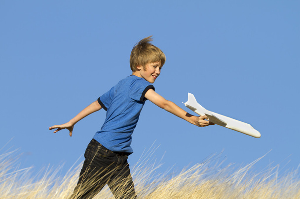 フィールドでおもちゃのグライダー飛行機で遊ぶ若い男の子 - 写真・画像