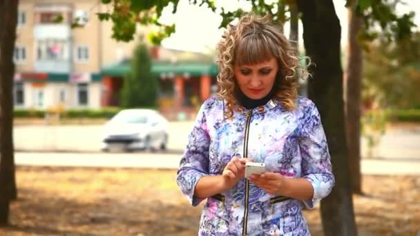 kobieta w średnim wieku pełne tłuszczu na telefon w parku za styl jazdy samochodów - Materiał filmowy, wideo