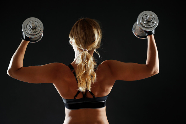athletische Frau mit Hanteln auf dunklem Hintergrund - Foto, Bild