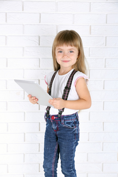 Little girl with tablet on brick wall background - Fotografie, Obrázek