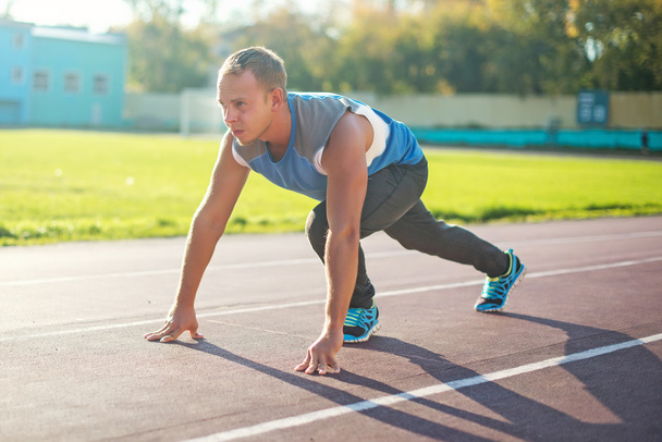 Homem atlético em pé em postura pronta para correr em uma esteira
 - Foto, Imagem