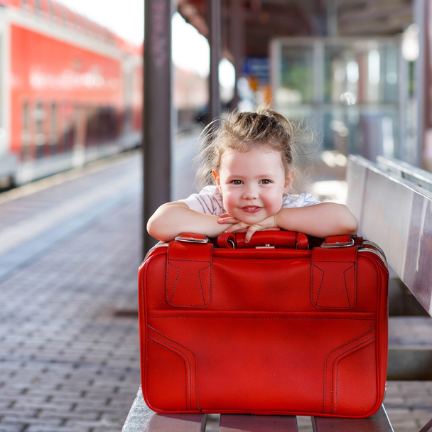 little girl with big red suitcase on a railway station - 写真・画像