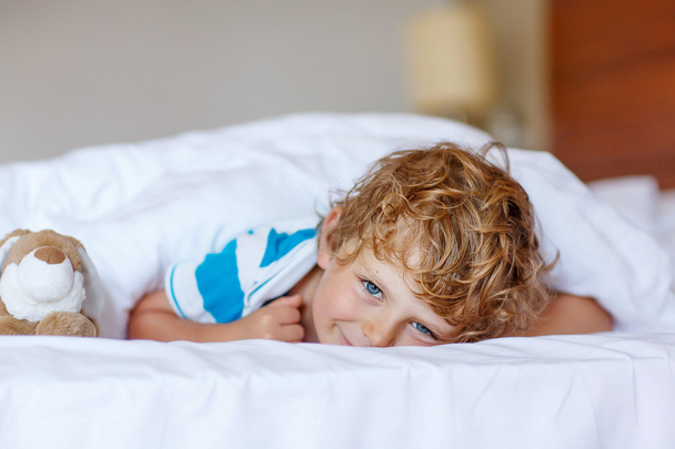 Suloinen lapsi poika nukkumisen jälkeen hänen valkoinen sänky lelu
 - Valokuva, kuva