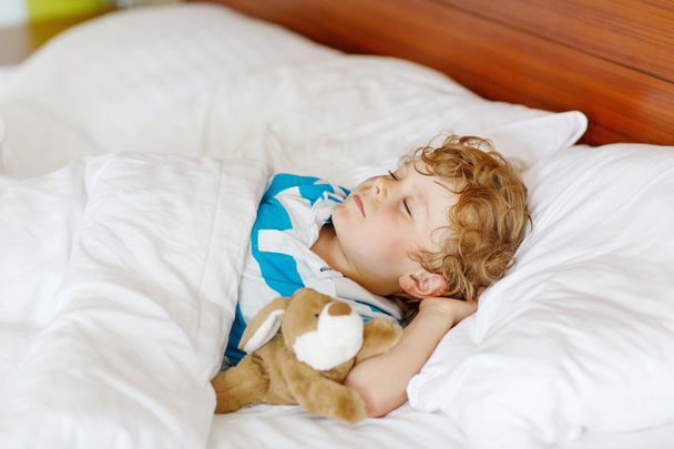 Pequeño niño rubio durmiendo en su cama con juguete
. - Foto, Imagen