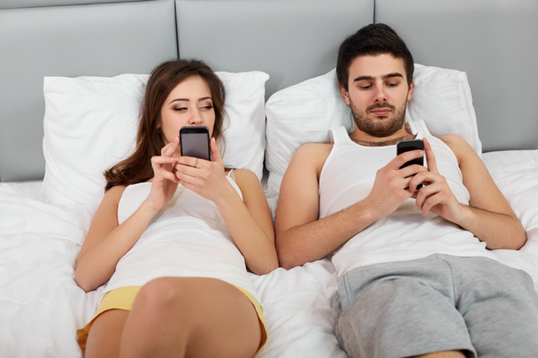 Happy Couple in a Bed with Mobile Phones - Valokuva, kuva
