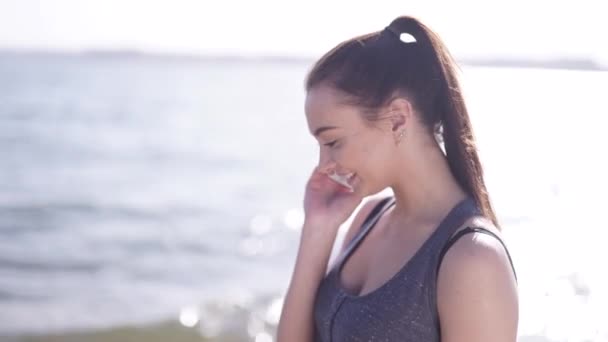Young athletic girl talking by phone on a beach - Felvétel, videó
