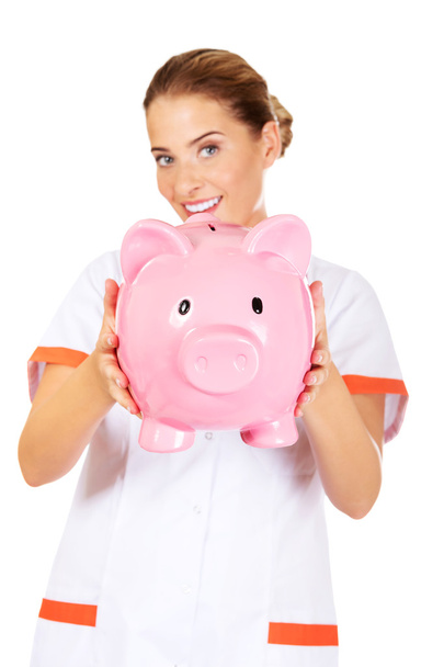 Young beautiful female doctor or nurse holding a piggybank - Foto, immagini