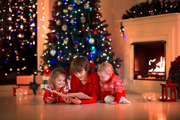 Kids reading a book on Christmas eve at fireplace - 写真・画像