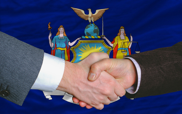 Frente a la bandera del estado americano de Nueva York dos hombres de negocios de la mano
 - Foto, Imagen