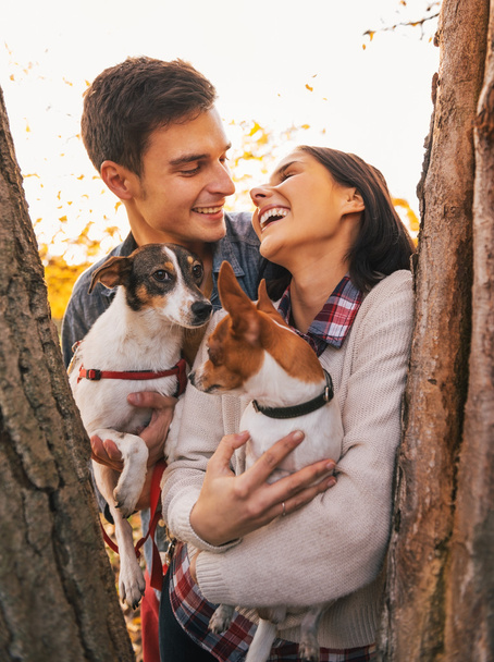 Happy young couple holding dogs in park and smiling - Foto, imagen
