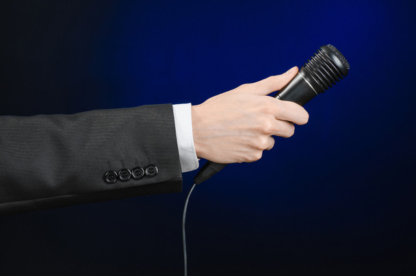 Business speech and topic: a man in a black suit holding a black microphone on a dark blue background in studio isolated - Fotoğraf, Görsel