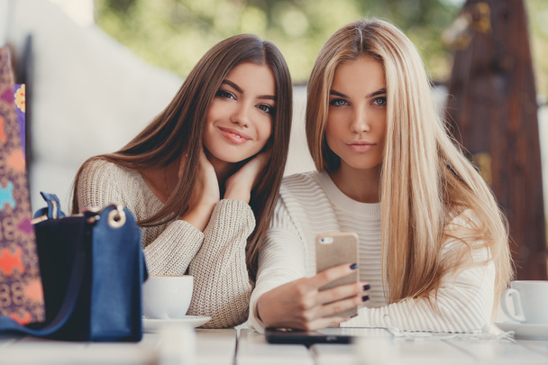 Two young women at cafe looking at pictures of new gadgets - Фото, изображение