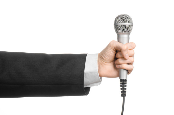 Business and speech topic: Man in black suit holding a gray microphone on an isolated white background in studio - Фото, изображение