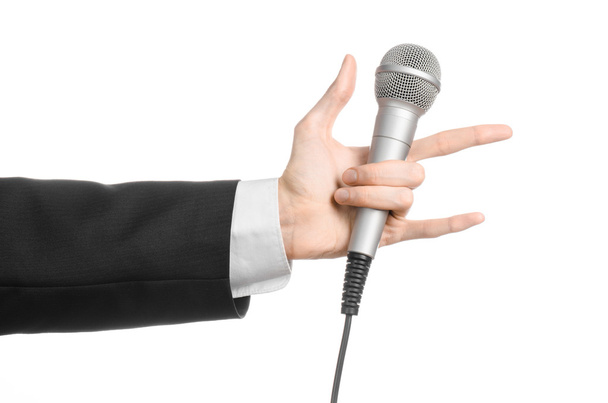 Business and speech topic: Man in black suit holding a gray microphone on an isolated white background in studio - Фото, изображение