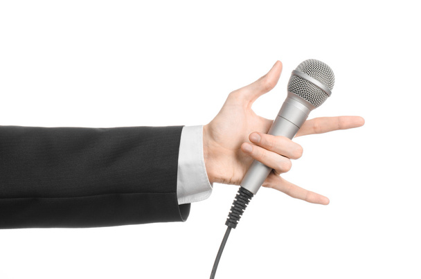 Business and speech topic: Man in black suit holding a gray microphone on an isolated white background in studio - Foto, Imagem