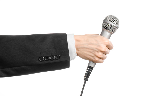 Business and speech topic: Man in black suit holding a gray microphone on an isolated white background in studio - 写真・画像