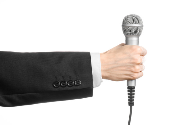 Business and speech topic: Man in black suit holding a gray microphone on an isolated white background in studio - Fotó, kép