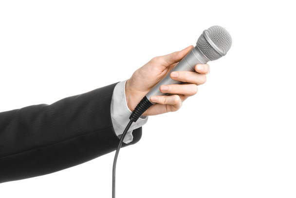 Business and speech topic: Man in black suit holding a gray microphone on an isolated white background in studio - Foto, immagini