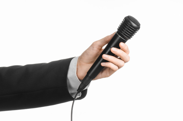 Business and speech topic: Man in black suit holding a black microphone isolated on white background in studio - Photo, Image