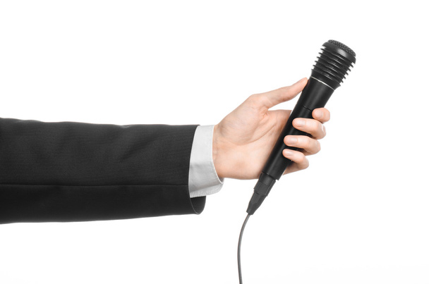 Business and speech topic: Man in black suit holding a black microphone isolated on white background in studio - Фото, изображение
